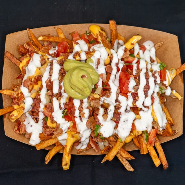 Loaded Jackpot fries with melted cheese, bacon, tomatoes, white sauce, and guacamole in a paper tray.