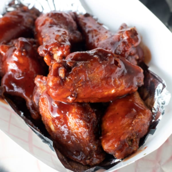 Close-up of Jackpot's American-style BBQ chicken wings, glistening with sauce in a foil-lined container.